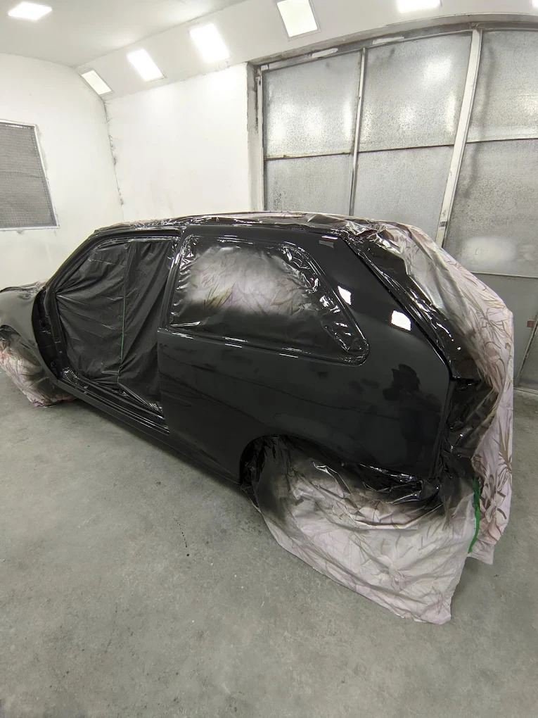 Carro preto mascarado dentro da cabine de pintura